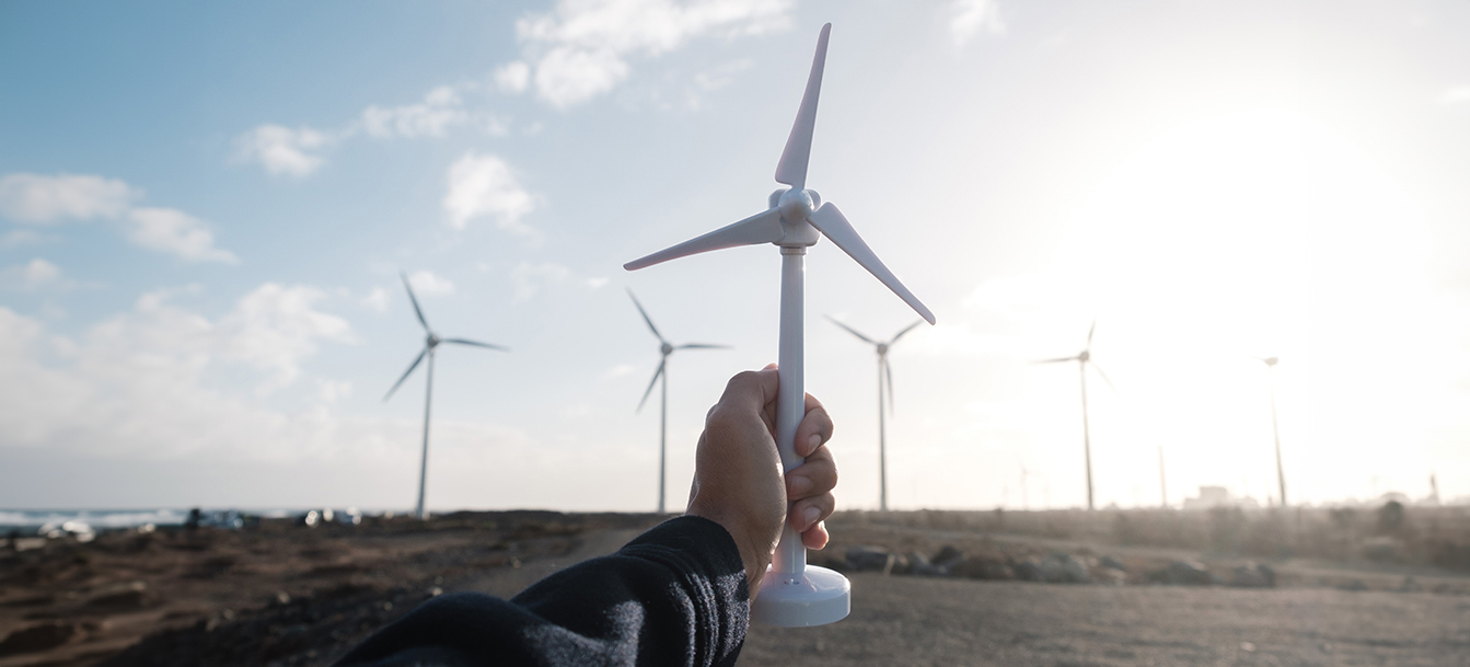 Mano sujetando juguete de molino de viento con fondo de campo de turbina de viento